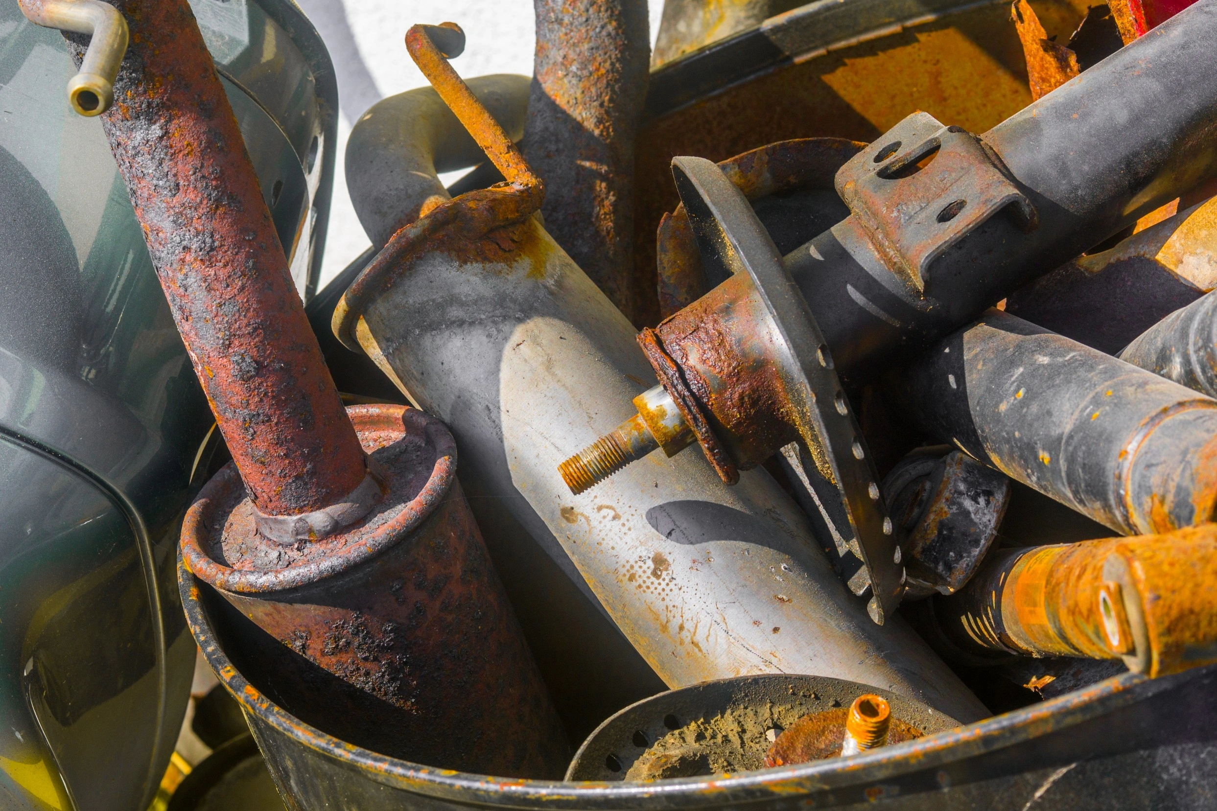 Used and rusty scrap catalytic converters and exhaust parts collected in a drum, ready for scrap catalytic converter buyers to weigh and recycle